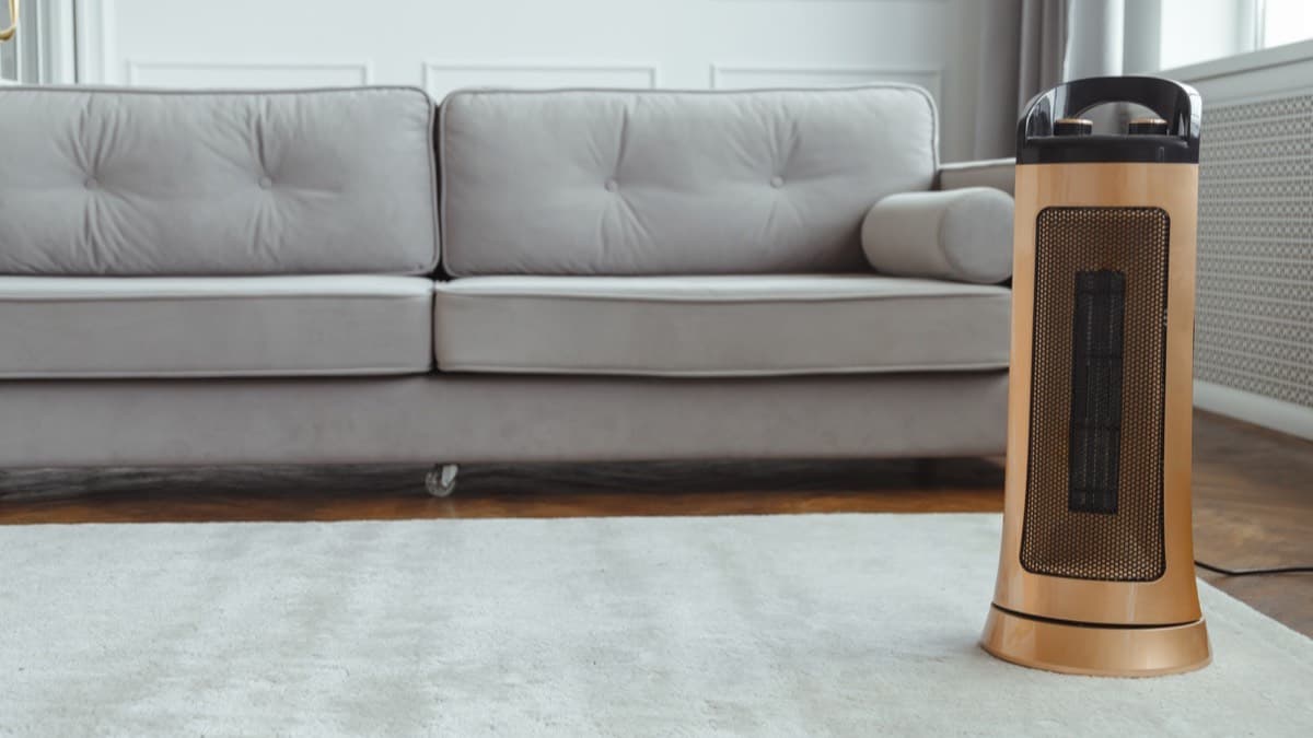 A ceramic tower space heater on a rug in front of a gray sofa