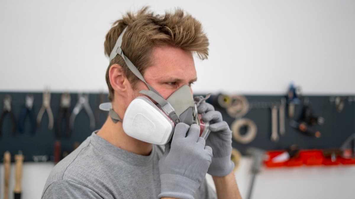 A worker in gloves adjusting a half-mask respirator in a workshop