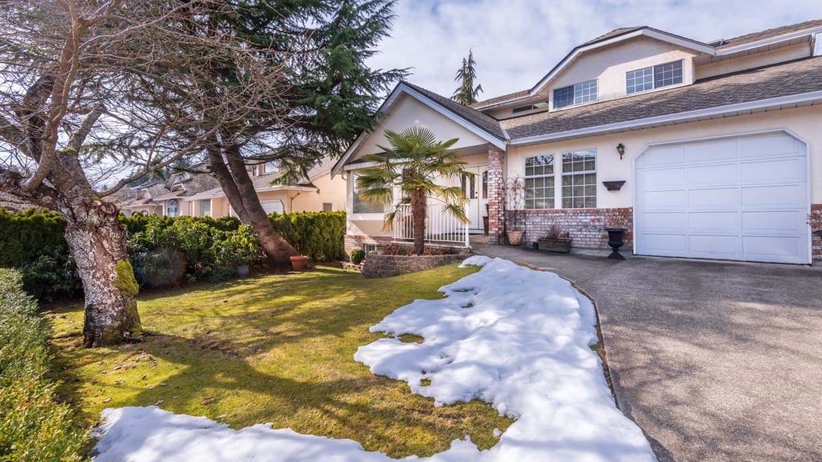 Melting snow banked along the edge of a driveway onto the front lawn of a house in early spring