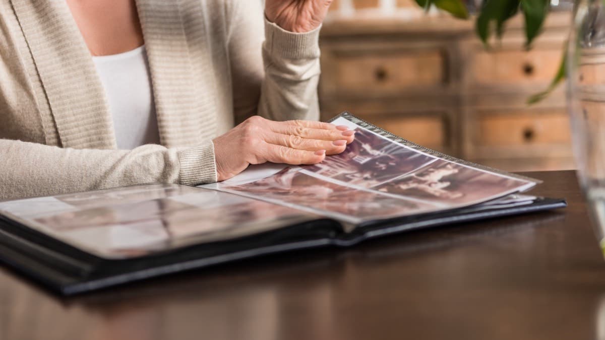 A person paging through a sleeved family photo album on a wooden table