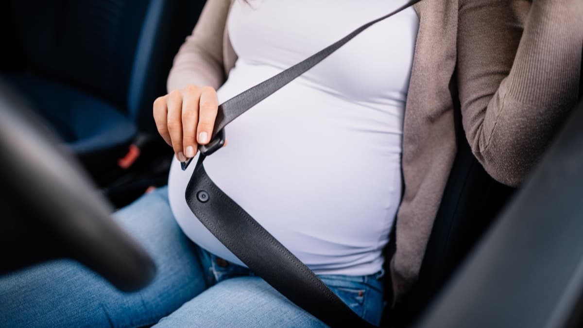 A pregnant driver drawing the seat belt across before buckling it
