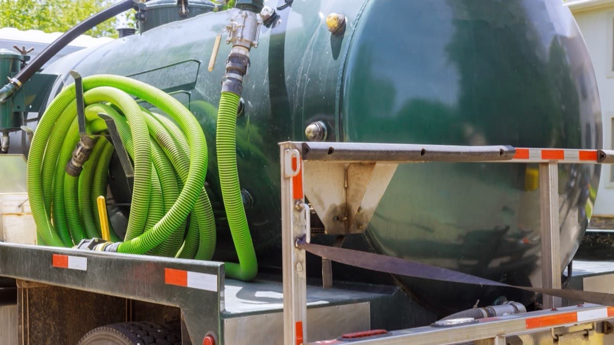 A septic pumping truck's green tank with coiled suction hose in a residential driveway