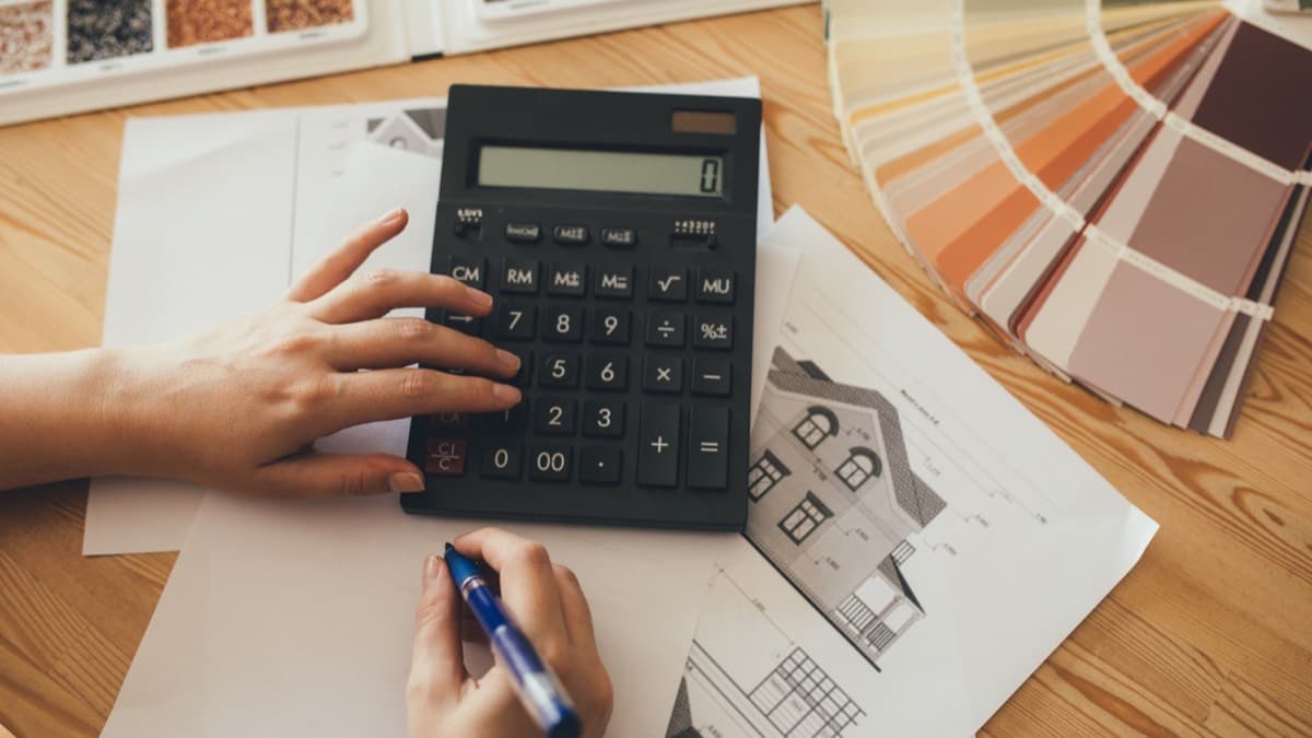 Hands working a calculator over house plans, with a paint color fan and finish samples on the table