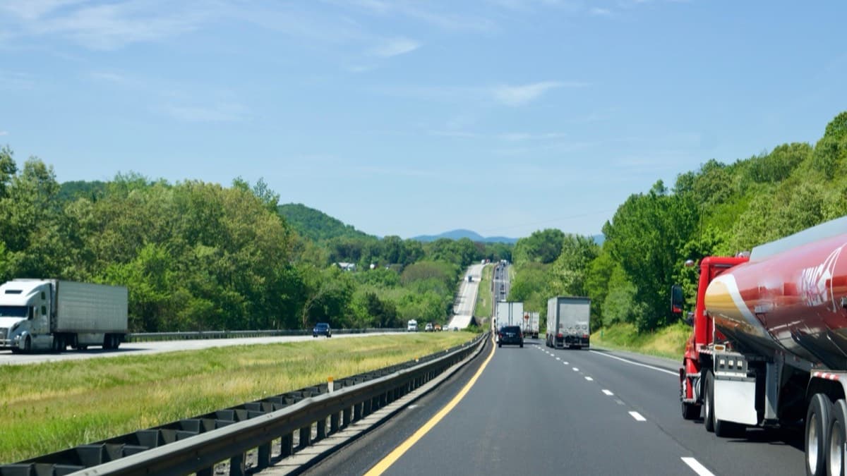 A driver's view of an interstate through green hills, with a tanker truck in the next lane and tractor-trailers ahead