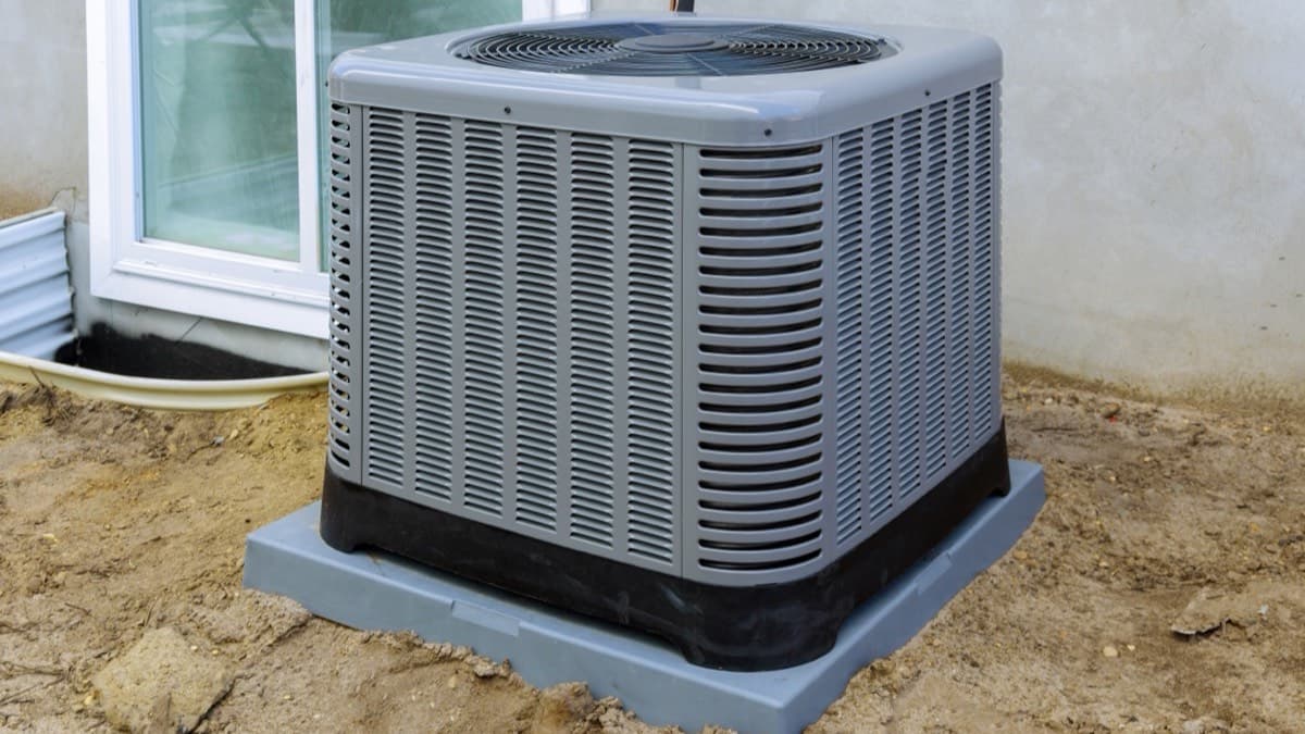 A newly installed air conditioner condenser on a fresh pad beside a house foundation