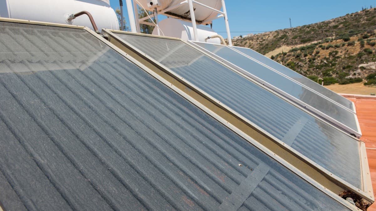 Flat glass solar water-heating collectors on a sunny roof, with storage tanks mounted above them