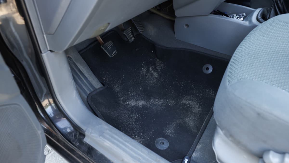 The open driver's door of a used car showing fine silt dried across the floor carpet and sill