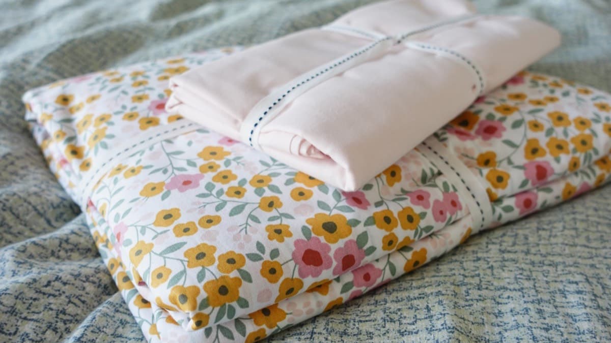 Folded floral and pink linens tied with ribbon on a bed