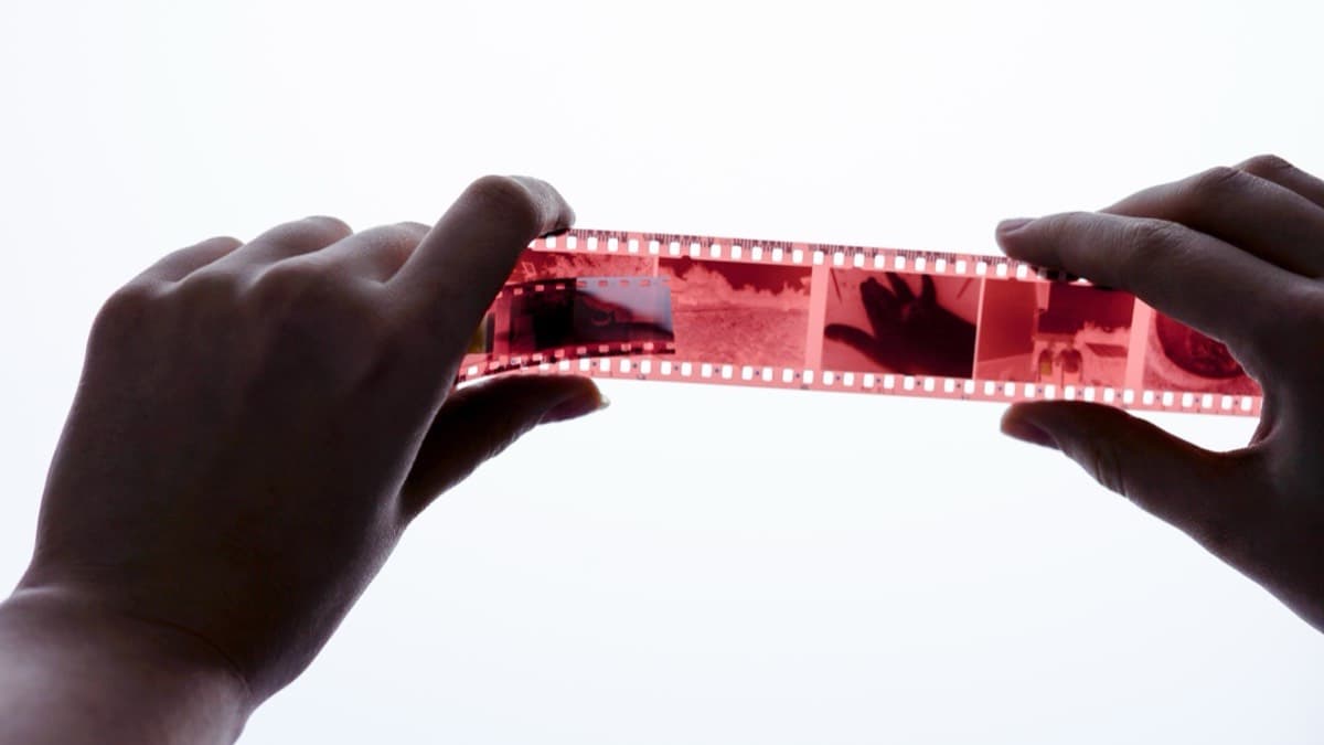 Hands holding a strip of color film negatives up to the light by its edges
