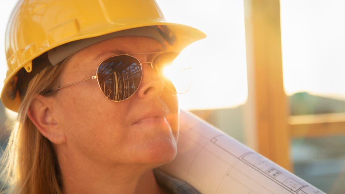 A worker in a hard hat and sunglasses in strong sun on a framing site