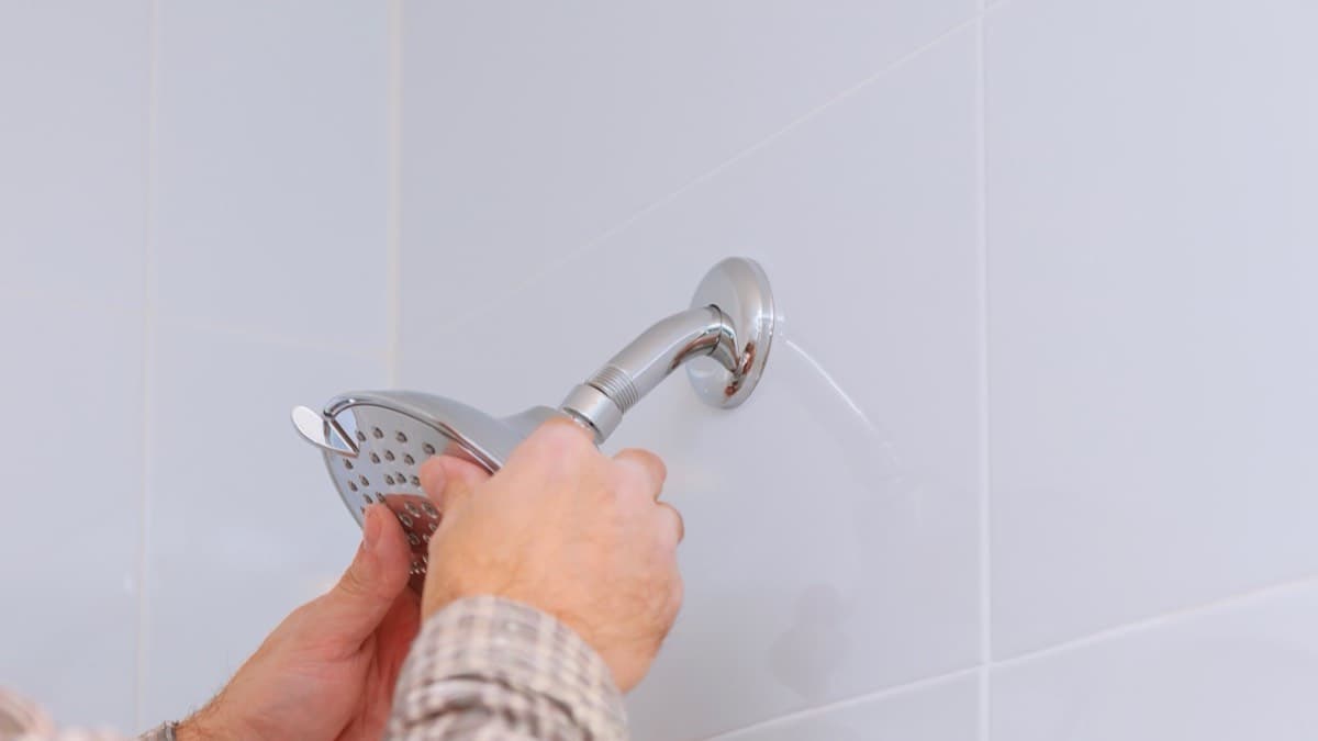 Hands threading a new chrome showerhead onto the shower arm