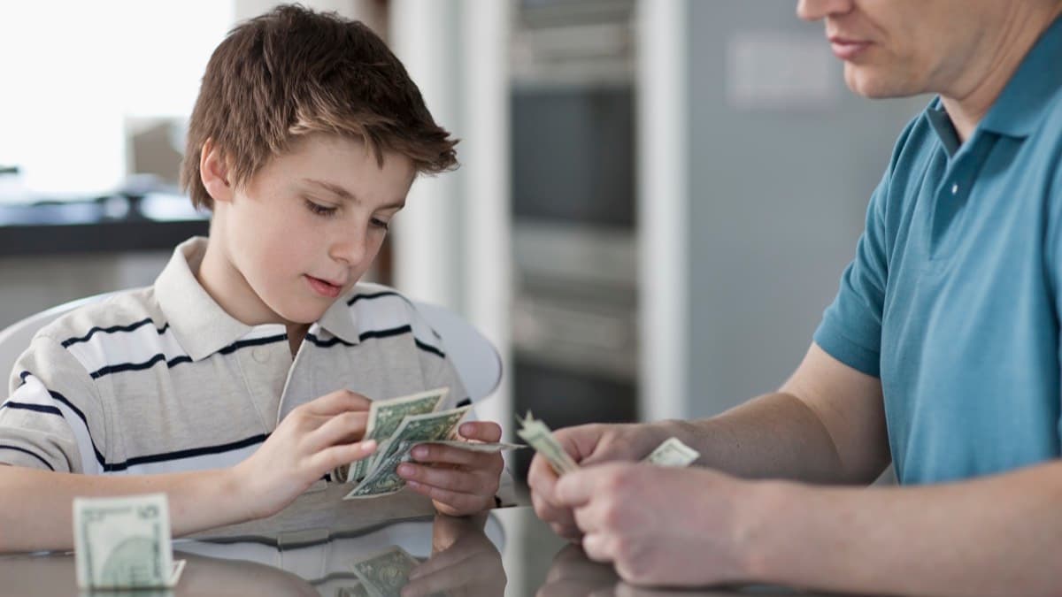A parent and a child counting dollar bills together at a kitchen table