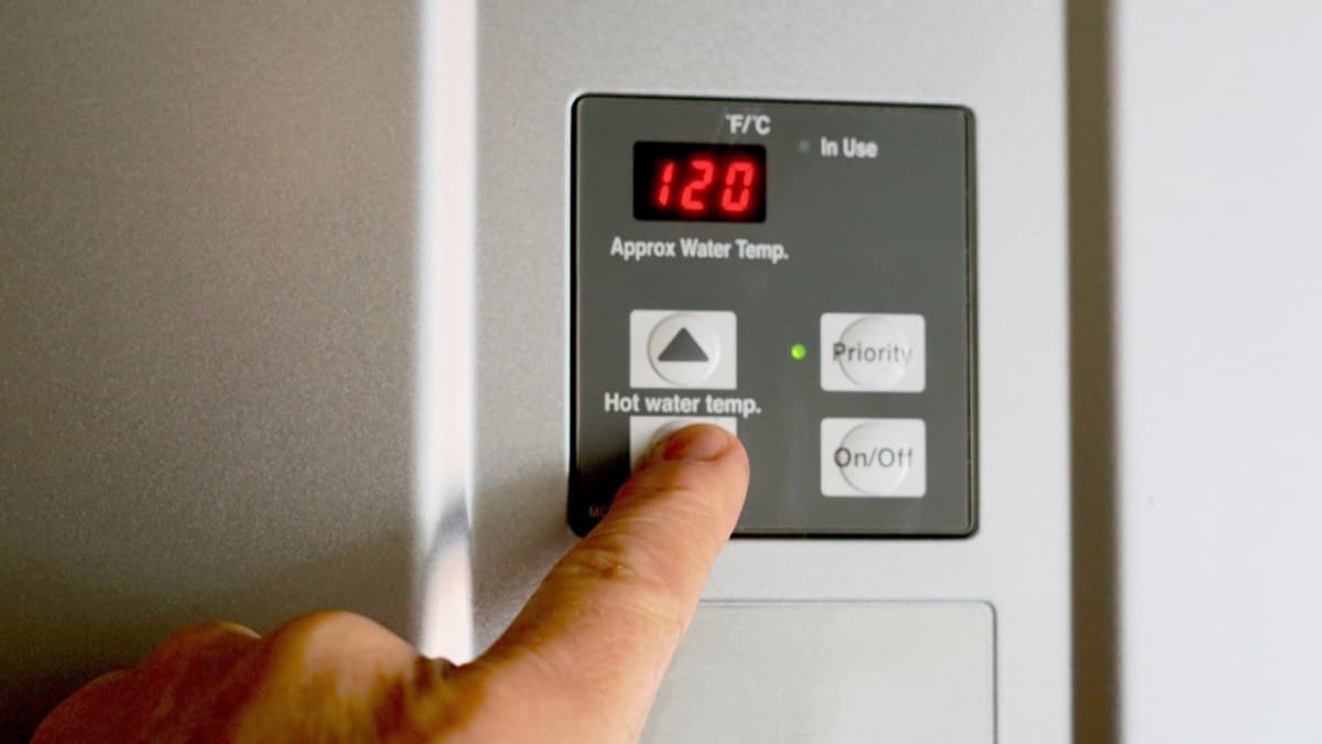A finger on the temperature button of a water heater control panel reading 120 degrees