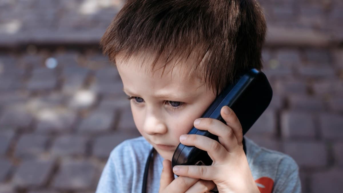 A young child holding a phone handset to one ear with a serious look