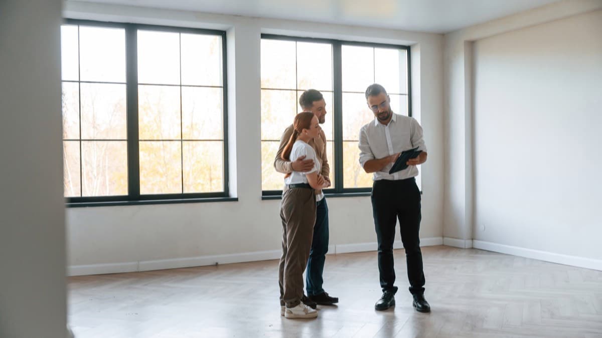 A couple and their agent reviewing a tablet in an empty sunlit room
