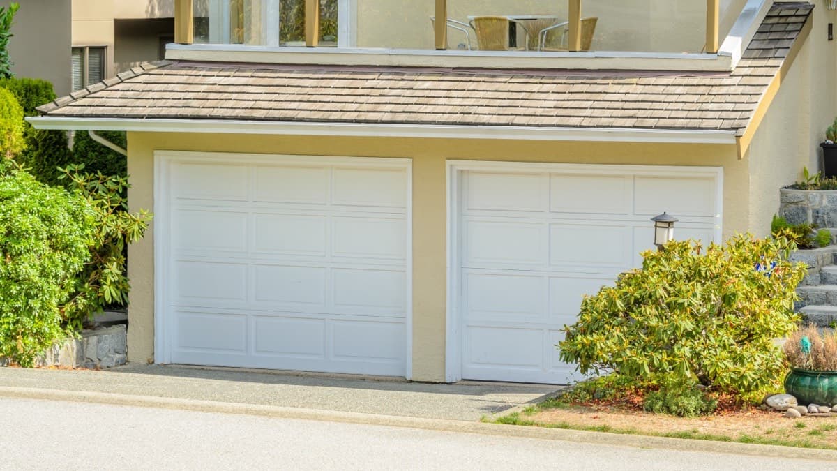 Two white overhead garage doors on a house beside the driveway