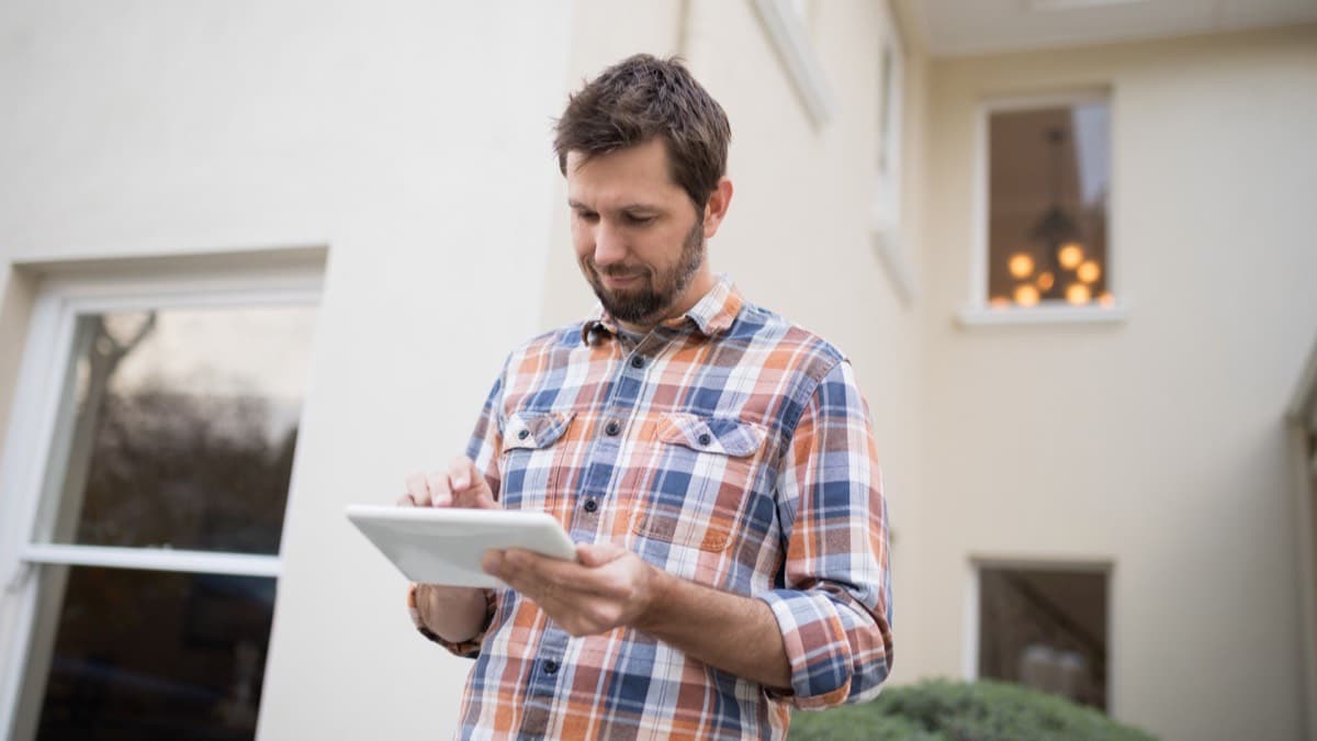 A homeowner checking a tablet while walking around the outside of the house