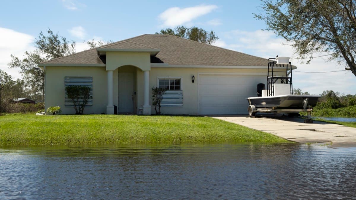 A single-story house with floodwater standing across the front lawn after a storm