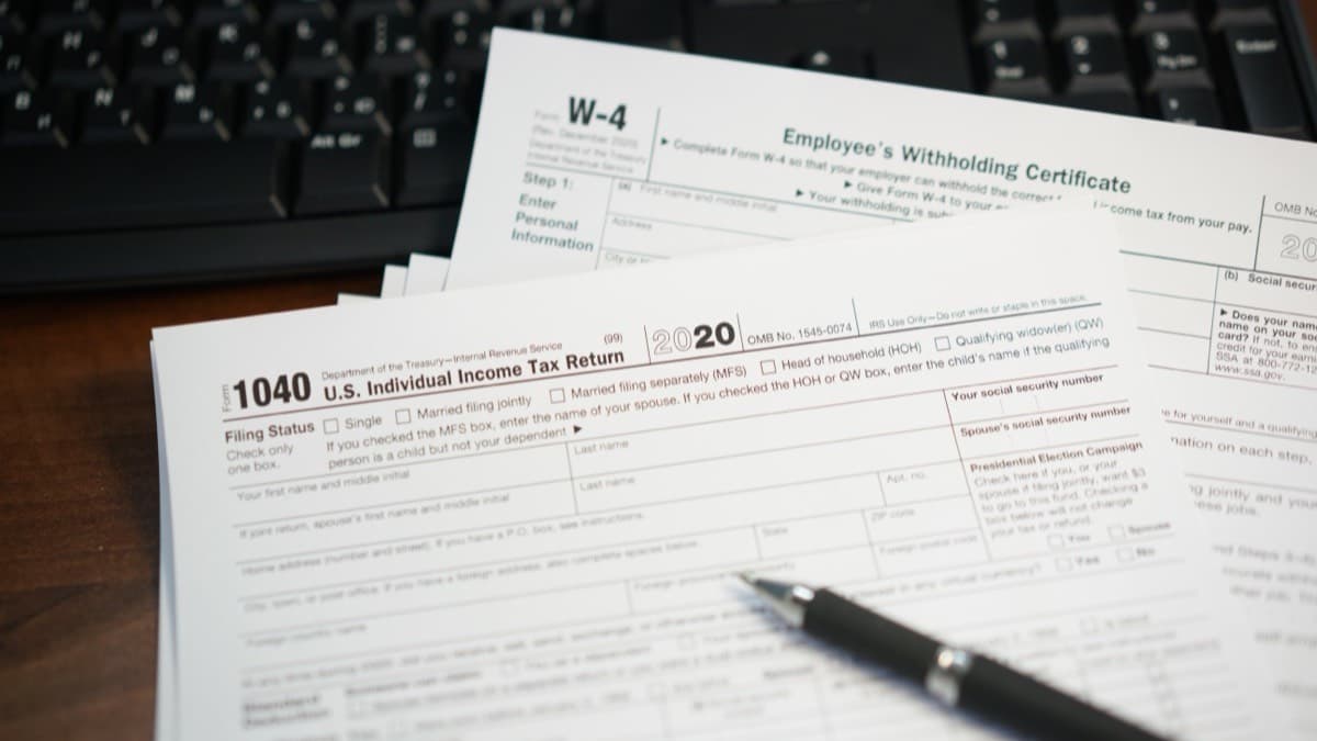 Federal income tax forms and a pen on a desk beside a keyboard