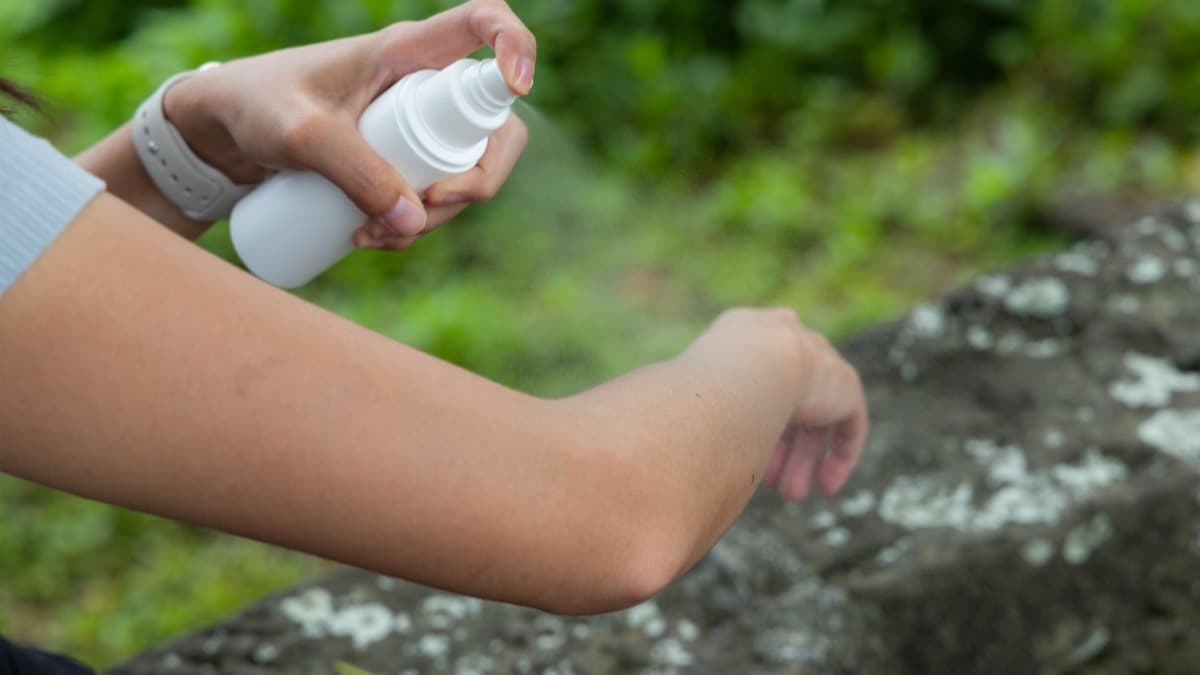 A person spraying insect repellent on their forearm outdoors