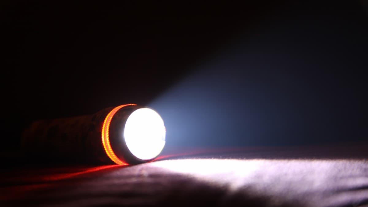 A flashlight lying on its side, its beam lighting a dark room