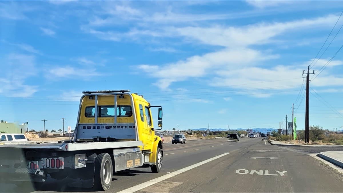 A flatbed tow truck driving on a sunny highway