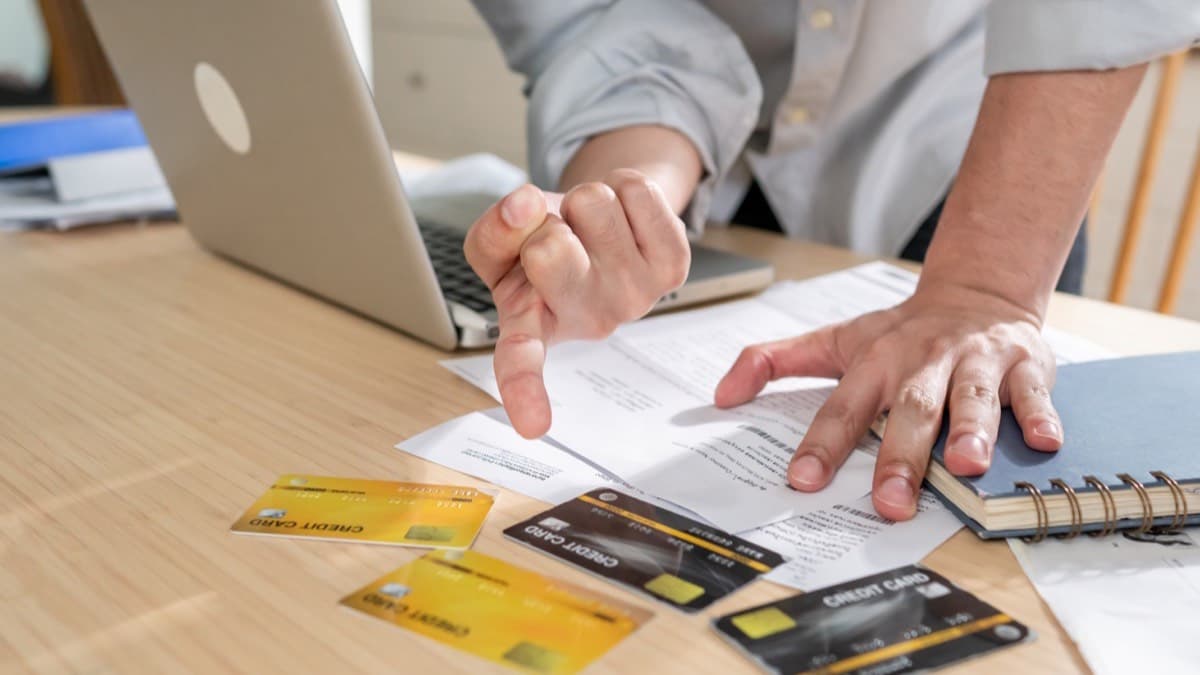A person going over bills at a desk with several credit cards spread beside a laptop