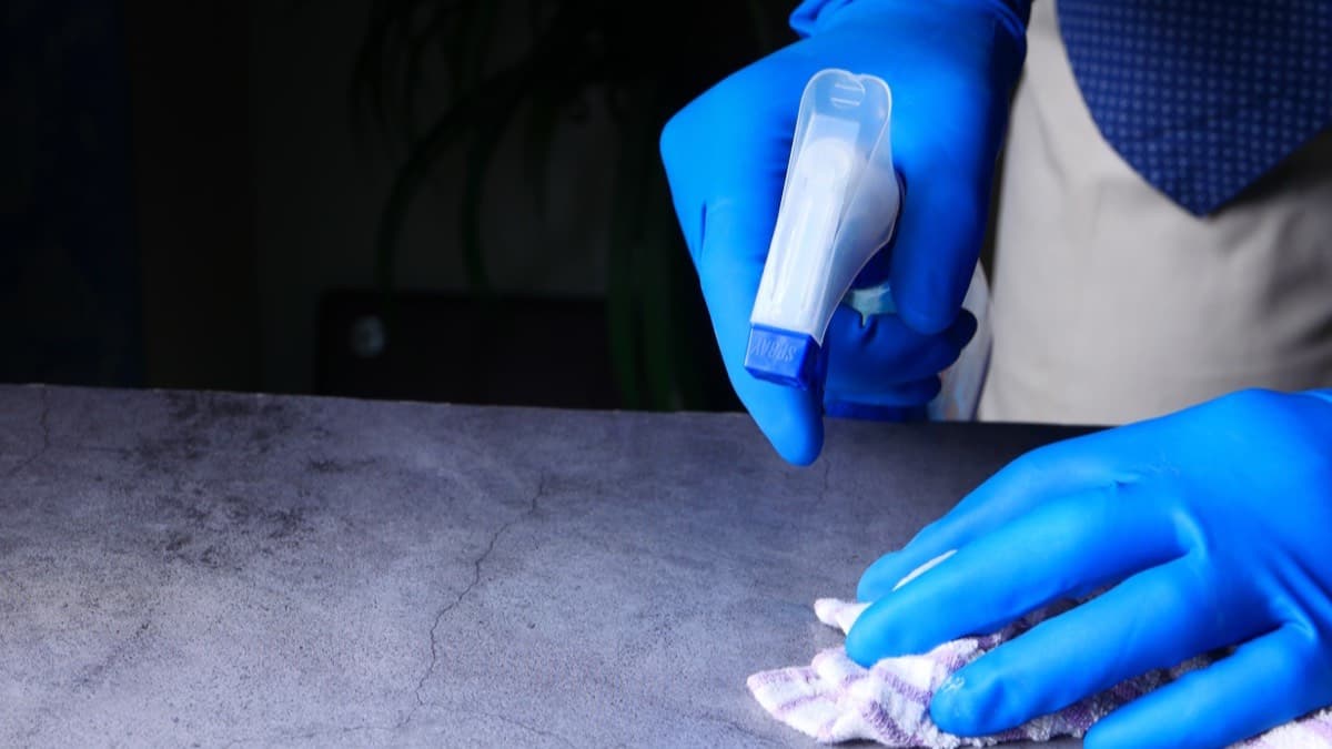 Gloved hands spraying a counter and wiping it with a cloth