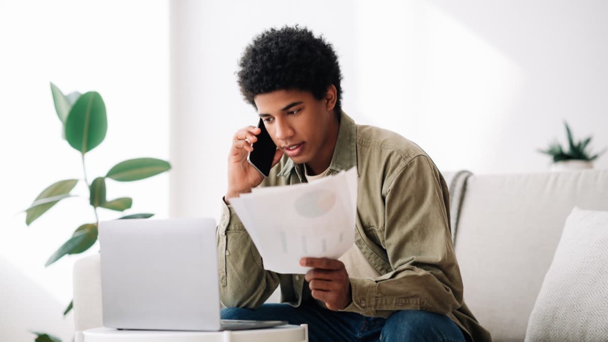 A young man on a phone call frowning at a bill in his hand