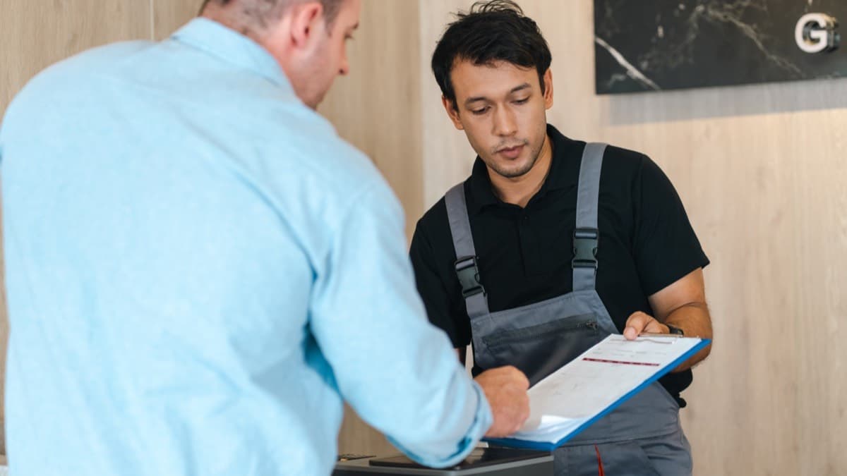 A service technician handing a customer a clipboard of paperwork to sign at the counter