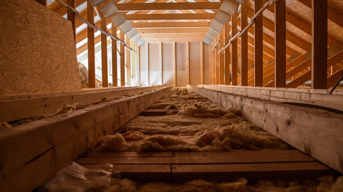 Loose insulation lying between the floor joists of an attic under wood rafters