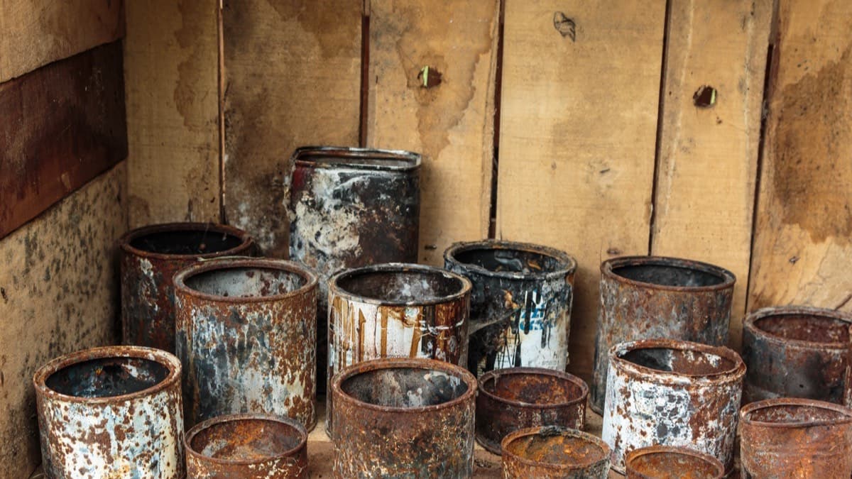 Old, rusted paint cans crowded together on a wooden shelf