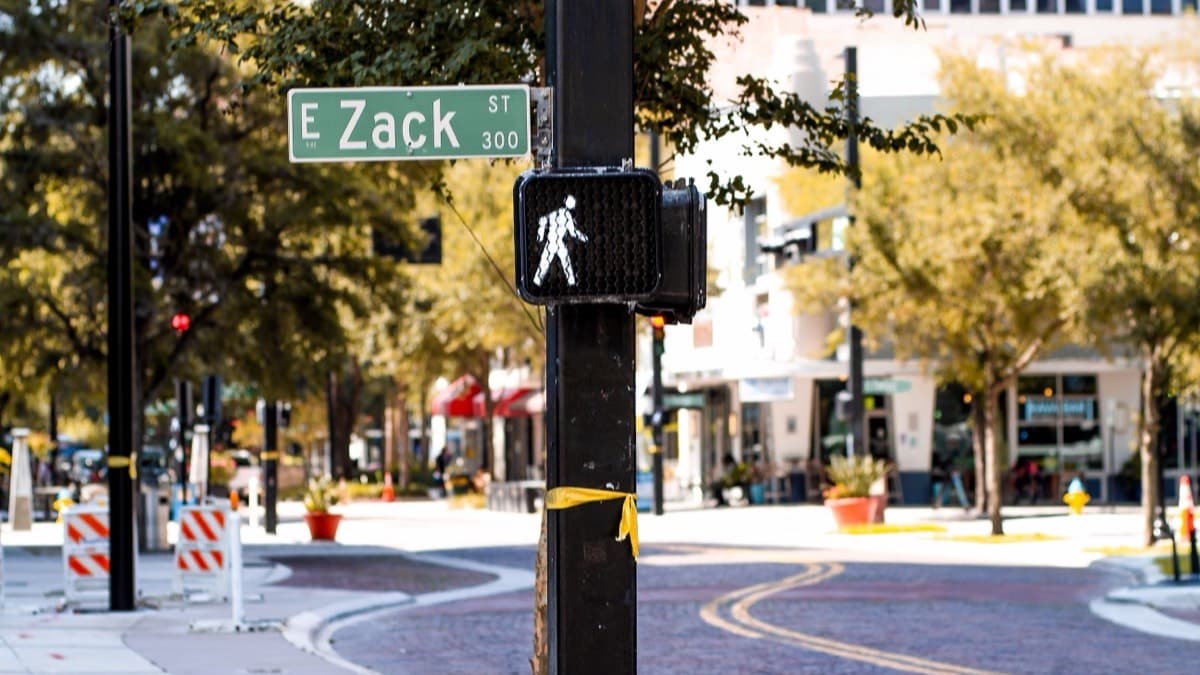 A lit walk signal on a pole at a downtown street corner