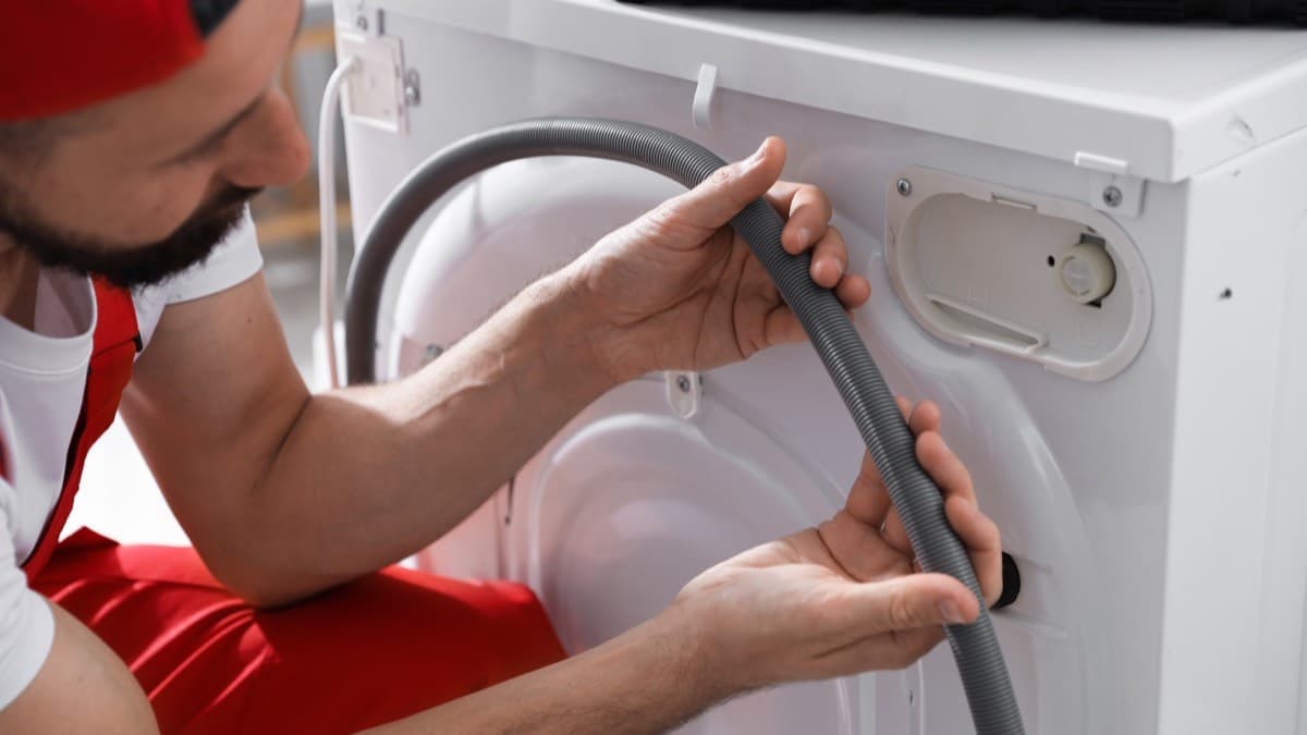 A repair technician fitting a hose to the back of a washing machine