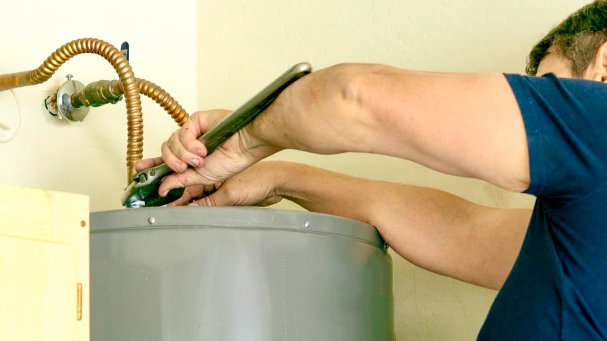 A person tightening a fitting on top of a tank water heater with a pipe wrench