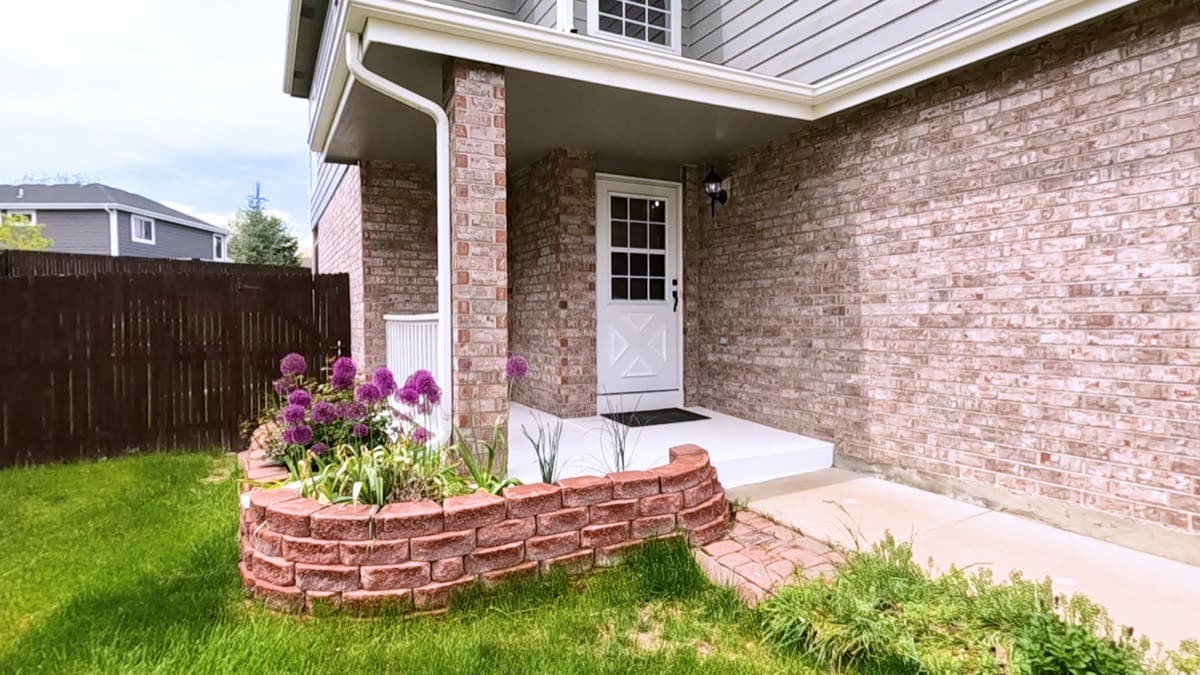 A brick house wall running down to a concrete step and lawn beside a curved brick planter