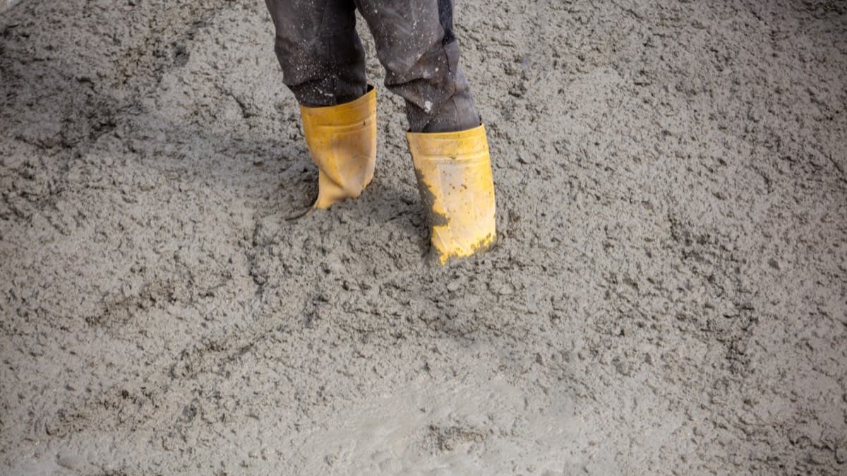 A worker in yellow rubber boots standing ankle-deep in freshly poured wet concrete