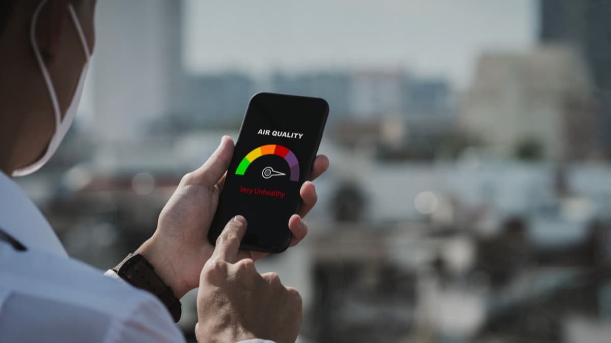 A phone showing a Very Unhealthy air quality reading held up against a hazy city view