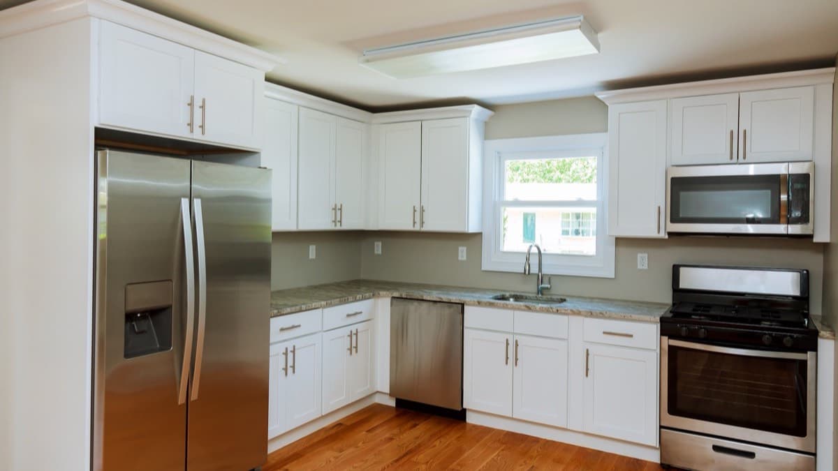 A kitchen with a stainless refrigerator, dishwasher, range and microwave under white cabinets