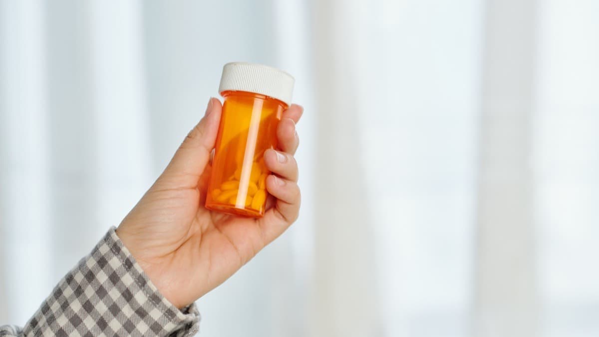 A hand holding up an orange prescription bottle of pills