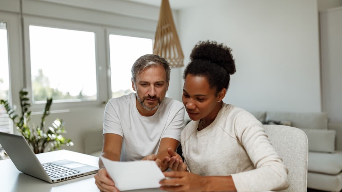Two adults at a table with a laptop reading a letter together