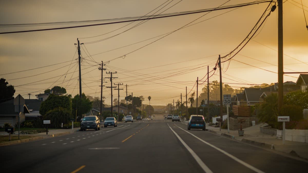 Cars on a neighborhood road lined with utility poles under a hazy amber sky