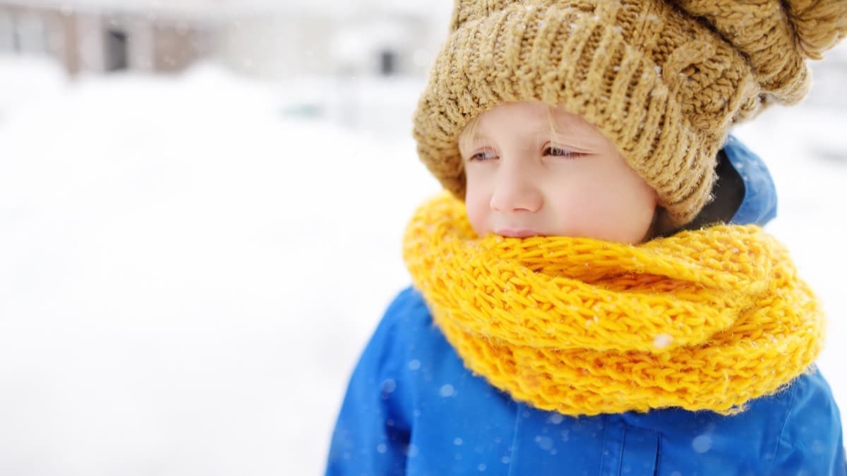 A young child bundled in a knit hat, thick yellow scarf and winter coat in falling snow