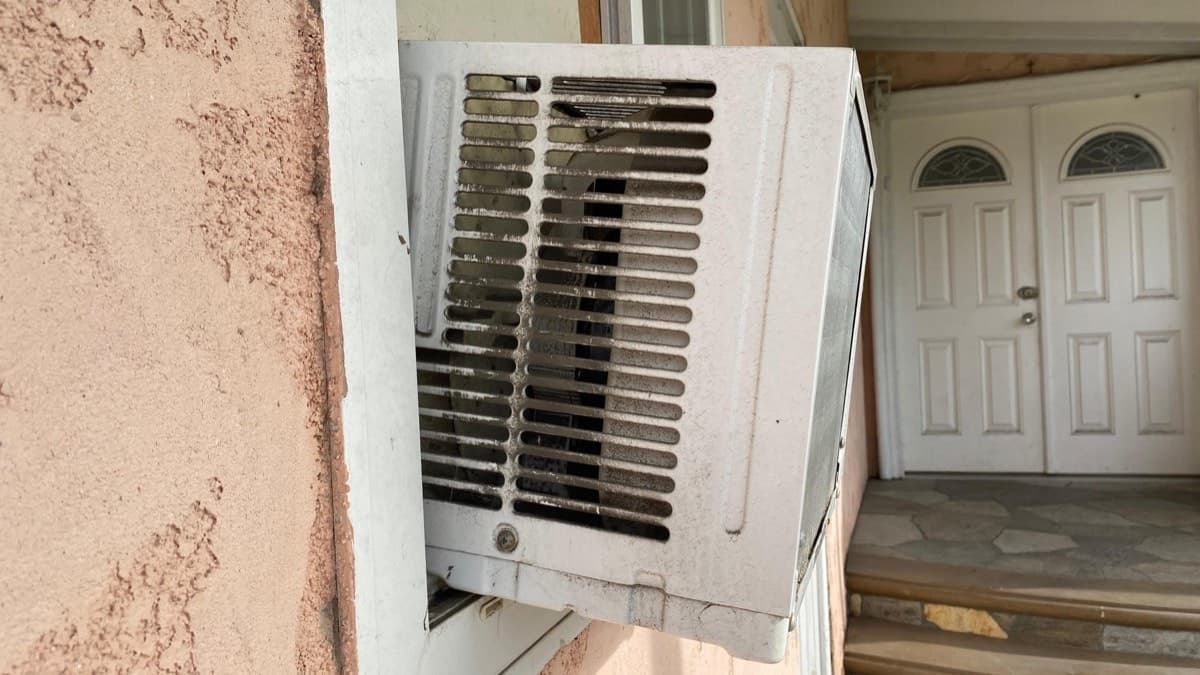 A window air conditioner unit sticking out of a stucco wall beside a front entry