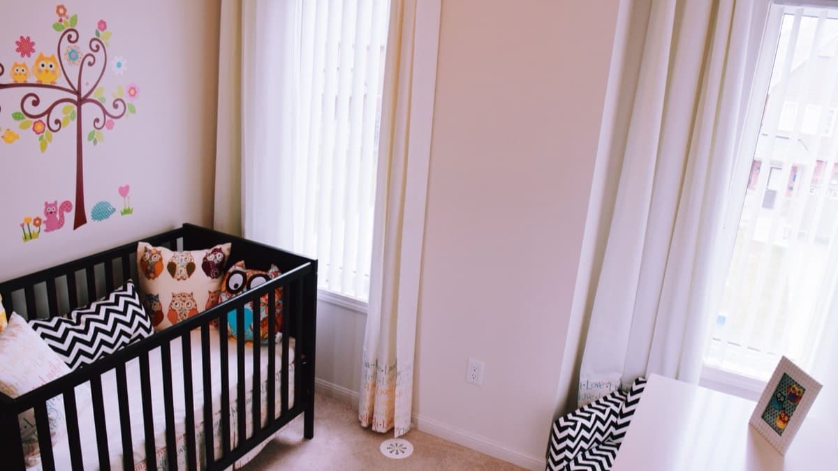 A nursery with a black crib a few feet from a window fitted with vertical blinds and curtains