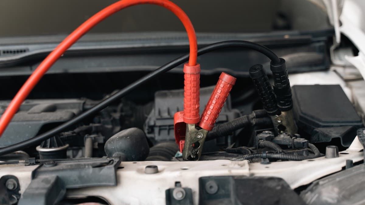 Red and black jumper cables clamped to a car battery under an open hood